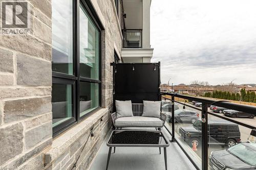Exterior balcony featuring a glass railing with a black metal top rail, a light gray stone facade, and a large black-framed window - 120 Springvalley Crescent Unit# 208, Hamilton, ON - Outdoor With Balcony With Exterior