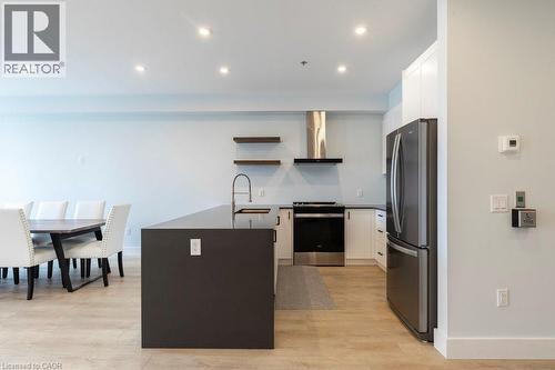 Modern open-concept kitchen featuring an oversized island with a built-in sink, stainless steel appliances, and wood-finish flooring - 120 Springvalley Crescent Unit# 208, Hamilton, ON - Indoor