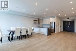 Open-concept living space featuring wood-finish flooring, recessed lighting, and a contemporary kitchen with white cabinetry, stainless steel appliances, and a central island with a sink - 