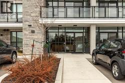 Modern building facade featuring a stone veneer exterior, expansive glass entrance doors, black-framed windows, and balconies with black railings - 