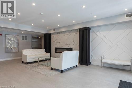 Lobby area featuring a modern fireplace with a stone-look surround, decorative wall paneling, recessed lighting, and tile flooring - 120 Springvalley Crescent Unit# 208, Hamilton, ON - Indoor With Fireplace