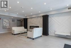 Lobby area featuring a modern fireplace with a stone-look surround, decorative wall paneling, recessed lighting, and tile flooring - 