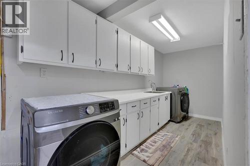 Laundry area featuring white cabinetry with black hardware, a utility sink, light-toned countertops, and wood-finish flooring - 168 Silver Aspen Crescent, Kitchener, ON - Indoor Photo Showing Laundry Room