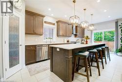 Kitchen featuring stainless steel dishwasher, an impressive center island + breakfast bar , decorative light fixtures, and backsplash - 