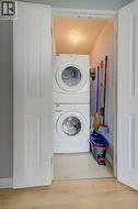 Laundry room featuring stacked washer / drying machine, a textured ceiling, and light wood-style floors - 