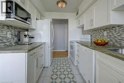 Virtually Staged  Kitchen with backsplash, white cabinets, white appliances, dark stone countertops, and light tile patterned floors - 