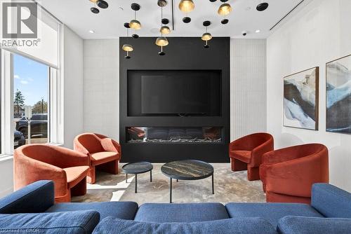 Contemporary living space featuring a built-in electric fireplace with a black surround, large format television recess, and a distinctive ceiling light installation - 500 Plains Road E Unit# 207, Burlington, ON - Indoor Photo Showing Living Room