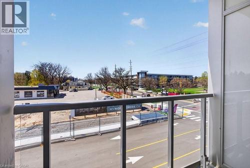 Balcony with glass railing and durable metal frame, offering an urban streetscape with commercial buildings and green spaces - 500 Plains Road E Unit# 207, Burlington, ON - Outdoor With Balcony