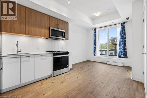 Modern kitchen with wood-finish upper cabinetry, white lower cabinetry, and stainless steel appliances - 500 Plains Road E Unit# 207, Burlington, ON - Indoor Photo Showing Kitchen