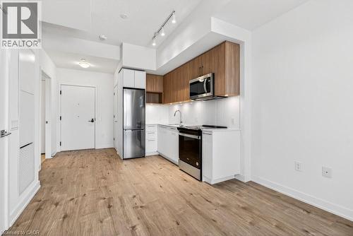 Compact kitchen featuring wood-finish upper cabinetry, white lower cabinetry, and stainless steel appliances - 500 Plains Road E Unit# 207, Burlington, ON - Indoor Photo Showing Kitchen With Stainless Steel Kitchen