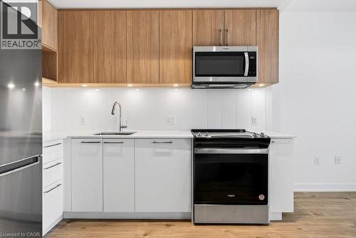 Modern kitchen featuring white cabinetry, wood-finish upper cabinets, stainless steel appliances, a white backsplash, and a contemporary faucet - 500 Plains Road E Unit# 207, Burlington, ON - Indoor Photo Showing Kitchen