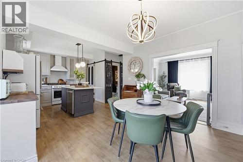 Open-concept kitchen and dining area featuring wood-finish flooring, a kitchen island with built-in dishwasher, stainless steel appliances, and a modern chandelier - 361 Cumberland Avenue, Hamilton, ON - Indoor Photo Showing Dining Room