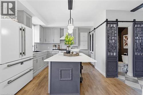 Gourmet kitchen featuring a central island with a white countertop, light gray cabinetry, built-in appliances, and wood-finish flooring - 361 Cumberland Avenue, Hamilton, ON - Indoor Photo Showing Kitchen