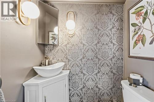 Powder room featuring striking patterned wallpaper, a white vessel sink atop a corner vanity, a wall-mounted mirror, and contemporary sconce lighting - 361 Cumberland Avenue, Hamilton, ON - Indoor Photo Showing Bathroom