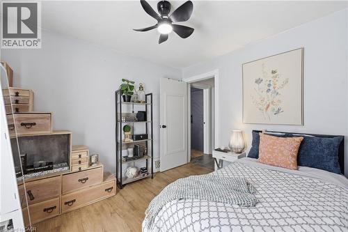 Light-filled room featuring wood-finish flooring, a modern black ceiling fan with integrated lighting, and a white paneled door - 361 Cumberland Avenue, Hamilton, ON - Indoor Photo Showing Bedroom