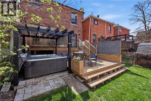 Backyard featuring a hot tub beneath a dark pergola, a multi-level wooden deck with integrated planter boxes, a manicured lawn, and brick exterior architecture - 361 Cumberland Avenue, Hamilton, ON - Outdoor With Deck Patio Veranda With Exterior