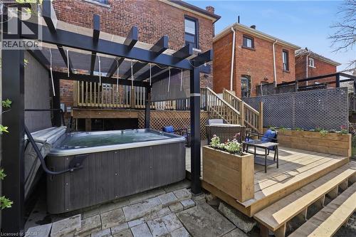 Outdoor entertainment area featuring a hot tub under a black pergola, a multi-level wooden deck with integrated planter boxes, and stone paver patio - 361 Cumberland Avenue, Hamilton, ON - Outdoor With Deck Patio Veranda With Exterior