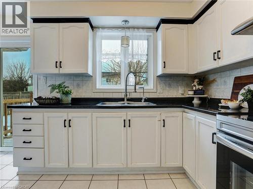 Kitchen featuring white cabinetry with black hardware, dark countertops, and a tiled backsplash - 154 Deerpath Drive, Guelph, ON - Indoor Photo Showing Kitchen With Double Sink