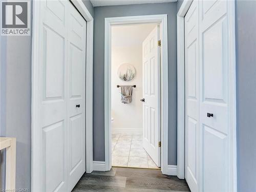 Hallway featuring two white bi-fold doors with black hardware, wood-finish flooring, and a gray wall color - 154 Deerpath Drive, Guelph, ON - Indoor Photo Showing Other Room