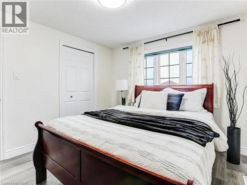 Bedroom featuring a large window with grid pattern, white baseboards, wood-finish flooring, a bi-fold closet door, and a flush-mount ceiling light fixture - 154 Deerpath Drive, Guelph, ON - Indoor Photo Showing Bedroom