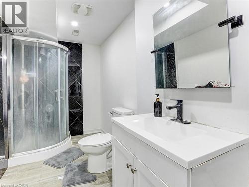 Bathroom featuring a curved glass shower enclosure, black geometric tile accent wall, white vanity with integrated sink, rectangular mirror, and wood-finish flooring - 154 Deerpath Drive, Guelph, ON - Indoor Photo Showing Bathroom
