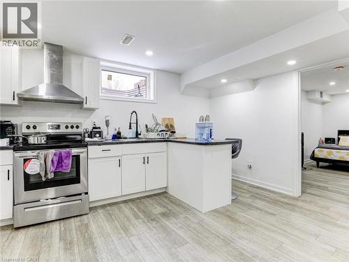 Kitchen featuring white cabinetry, stainless steel range with hood vent, black countertops, and wood-finish flooring - 154 Deerpath Drive, Guelph, ON - Indoor Photo Showing Kitchen