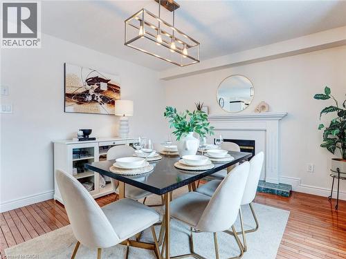 Dining area featuring a decorative fireplace with a mantel, a rectangular chandelier, hardwood flooring, and a white built-in console cabinet with glass doors - 154 Deerpath Drive, Guelph, ON - Indoor Photo Showing Dining Room With Fireplace