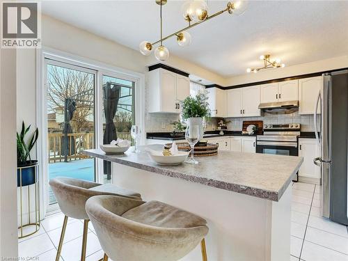Kitchen featuring a breakfast bar with a stone-finish countertop, white cabinetry with black trim, stainless steel appliances, and a tiled backsplash - 154 Deerpath Drive, Guelph, ON - Indoor Photo Showing Kitchen With Upgraded Kitchen