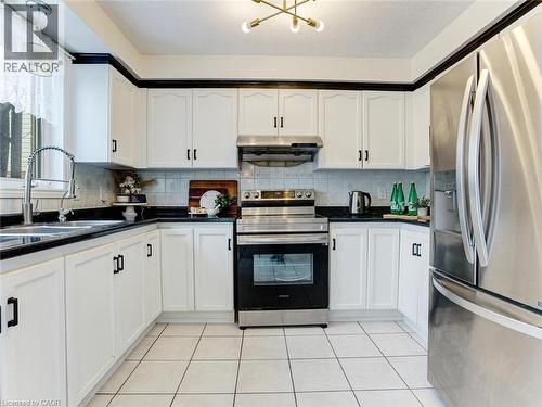 U-shaped kitchen featuring white cabinetry with black trim, black countertops, and a tile backsplash - 154 Deerpath Drive, Guelph, ON - Indoor Photo Showing Kitchen
