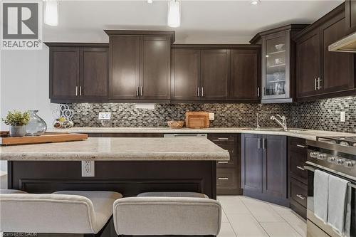 Kitchen featuring dark wood-finish cabinetry with brushed nickel hardware, a mosaic tile backsplash, and light-toned countertops - 7 Gibson Place Unit# 26, St. Catharines, ON - Indoor Photo Showing Kitchen With Upgraded Kitchen