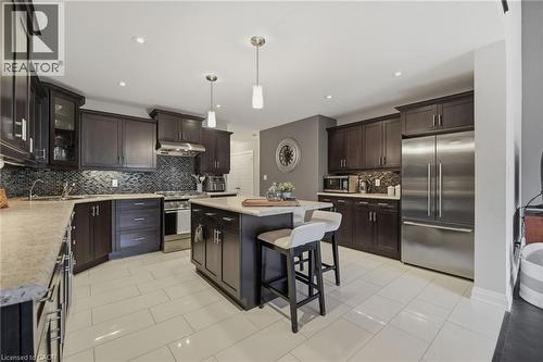 Kitchen featuring dark wood cabinetry, stainless steel appliances, a mosaic tile backsplash, a central island with countertop seating, and light-toned tile flooring - 7 Gibson Place Unit# 26, St. Catharines, ON - Indoor Photo Showing Kitchen With Stainless Steel Kitchen With Upgraded Kitchen