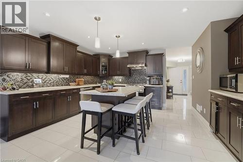 Kitchen featuring dark wood cabinetry, light-toned countertops, a mosaic tile backsplash, a central island with seating, and light-toned tile flooring - 7 Gibson Place Unit# 26, St. Catharines, ON - Indoor