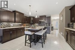 Kitchen featuring dark wood cabinetry, light-toned countertops, a mosaic tile backsplash, a central island with seating, and light-toned tile flooring - 