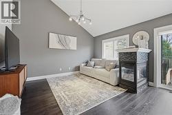 Living area featuring vaulted ceilings, dark wood-finish flooring, a contemporary fireplace with tile surround, white plantation shutters, and glass sliding doors leading to an exterior deck - 