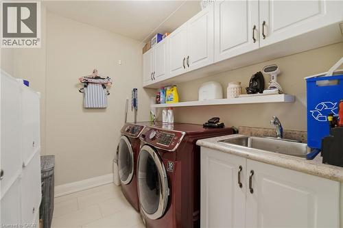 Dedicated laundry area featuring a stainless steel sink, ample cabinet storage, a floating shelf, and neutral wall tones - 7 Gibson Place Unit# 26, St. Catharines, ON - Indoor Photo Showing Laundry Room