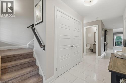 Entryway featuring white rectangular tile flooring, a staircase with carpeted treads and a black handrail, a double-panel white closet door, and a recessed powder room with a vanity and toilet - 7 Gibson Place Unit# 26, St. Catharines, ON - Indoor Photo Showing Other Room