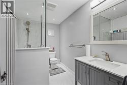 Contemporary bathroom featuring a glass-enclosed shower with white marble-look tile, a grey vanity with a white countertop and integrated sink, a large framed mirror, and recessed ceiling lighting - 