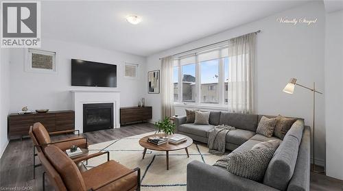 Bright living area featuring wood-finish flooring, a contemporary fireplace with a white mantel, and extensive window space - 123 Rea Drive, Fergus, ON - Indoor Photo Showing Living Room With Fireplace
