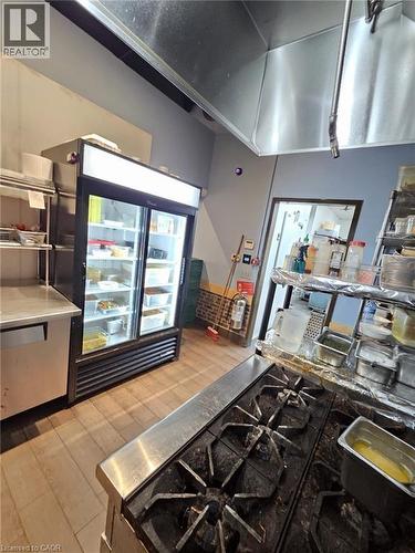 Commercial kitchen featuring a stainless steel range, professional-grade refrigerator, wood-finish flooring, and industrial ventilation hood - 4322 Ontario Street Unit# 1, Lincoln, ON 