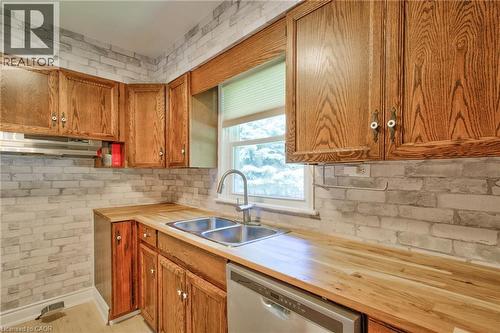 Kitchen featuring wood cabinetry, butcher block countertops, stainless steel double basin sink, stainless steel faucet, and white brick-patterned backsplash - 31 Brodick Street, Hamilton, ON - Indoor Photo Showing Kitchen With Double Sink