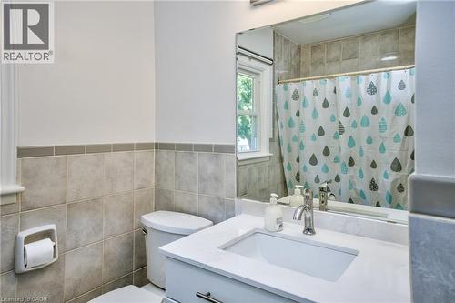 Bathroom featuring a vanity with an integrated sink and light-toned countertop, a polished chrome faucet, a large wall-mounted mirror, and a toilet - 31 Brodick Street, Hamilton, ON - Indoor Photo Showing Bathroom