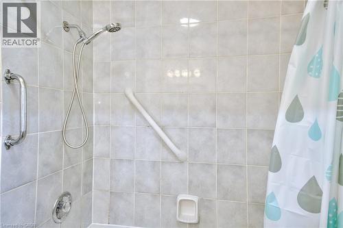 Shower enclosure featuring light-toned square wall tiles, a chrome hand-held showerhead, a chrome wall-mounted grab bar, and a white angled grab bar - 31 Brodick Street, Hamilton, ON - Indoor Photo Showing Bathroom