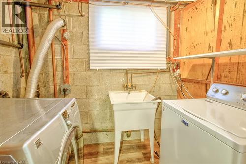 Utility room featuring concrete block walls, a laundry sink, and wood-finish flooring - 31 Brodick Street, Hamilton, ON - Indoor Photo Showing Laundry Room