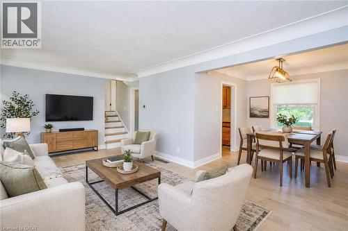 Open-concept living and dining areas featuring light wood-finish flooring, a contemporary light fixture, and a staircase with white risers and wood treads - 31 Brodick Street, Hamilton, ON - Indoor Photo Showing Living Room