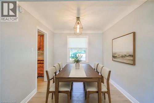 Dedicated dining area featuring wood-finish flooring, a contemporary geometric pendant light, and a window with a roller shade - 31 Brodick Street, Hamilton, ON - Indoor Photo Showing Dining Room