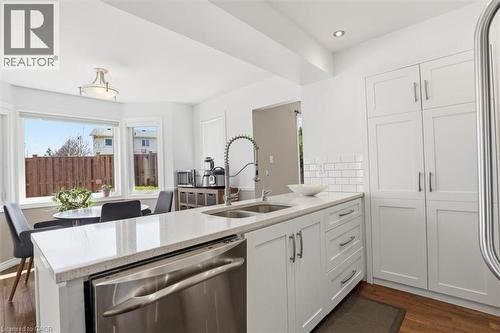 Modern kitchen featuring an island with a light-toned countertop, a stainless steel dishwasher, and a double basin sink with a pull-down faucet - 113 Glenecho Court, Waterloo, ON - Indoor Photo Showing Kitchen With Double Sink