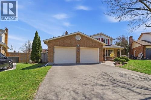 Brick exterior residence featuring a two-car garage, paved driveway, covered front porch, and established landscaping - 113 Glenecho Court, Waterloo, ON - Outdoor