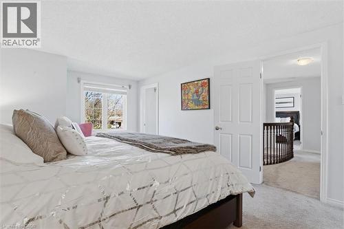 Carpeted bedroom with a window featuring white blinds, a white paneled door, and a brown wooden railing visible through an open doorway - 113 Glenecho Court, Waterloo, ON - Indoor Photo Showing Bedroom