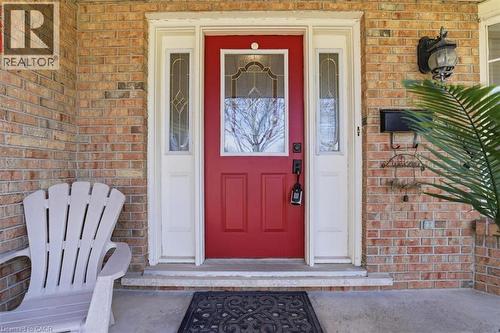 Brick facade entrance featuring a red front door with decorative glass, two sidelight windows, a wall-mounted exterior light fixture, and a black mailbox - 113 Glenecho Court, Waterloo, ON - Outdoor With Exterior