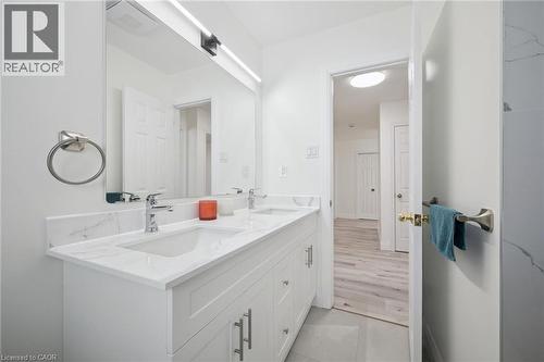Double vanity with integrated sinks and a light-toned countertop, set against a full-width mirror with linear overhead lighting - 27 Silverspring Crescent, Kitchener, ON - Indoor Photo Showing Bathroom